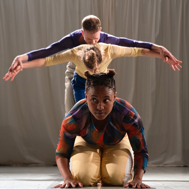 Vier Performer*innen stehen im Kreis und halten sich an den Händen, eine Szene aus einer zeitgenössischen Tanzperformance mit Fokus auf Gemeinschaft.