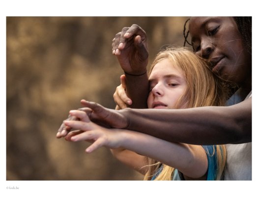 Two persons perform a shared arm movement. Four arms overlap in the foreground, forming a dense composition of hands and lines. The blurred background keeps attention on the gesture.
